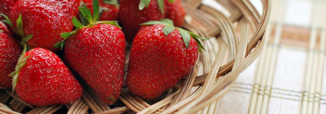 Rijpe aardbeien in een gevlochten mand op een geruit tafelkleed.