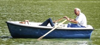 Oudere man roeit in een blauwe roeiboot met een passagier.