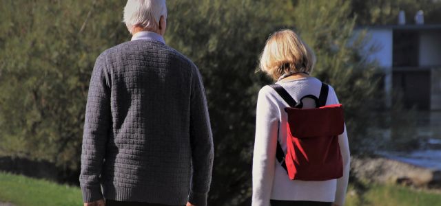 Oudere man en vrouw wandelen samen, de vrouw met een rode rugzak.