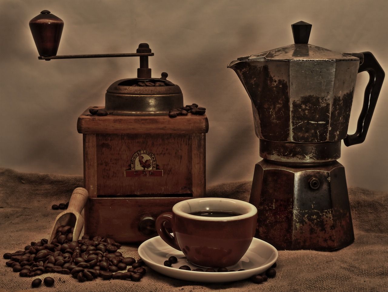 Een oude koffiemolen, een koffiepot en een kop zwarte koffie tussen verspreide koffiebonen.