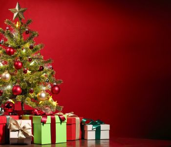 Een versierde kerstboom met ingepakte cadeaus op een rode achtergrond.
