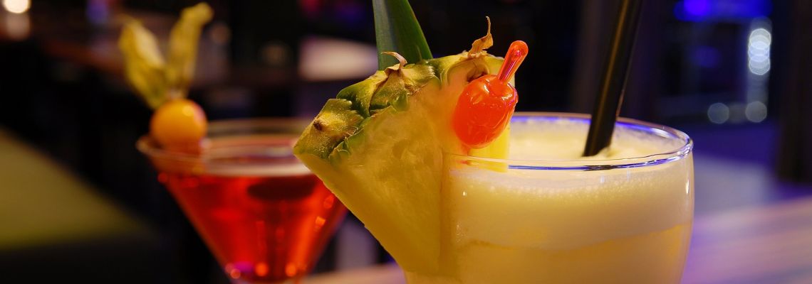 Twee cocktails, met vooraan een romig geel drankje versierd met ananas en een kers.