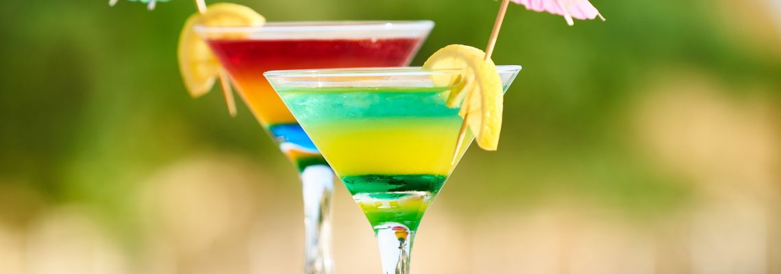 Kleurrijke cocktails in laagjes, versierd met citroen en papieren parasolletjes.