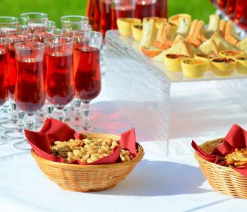 Glazen met rode aperitiefdrank, mandjes met nootjes en hapjes op een tafel.