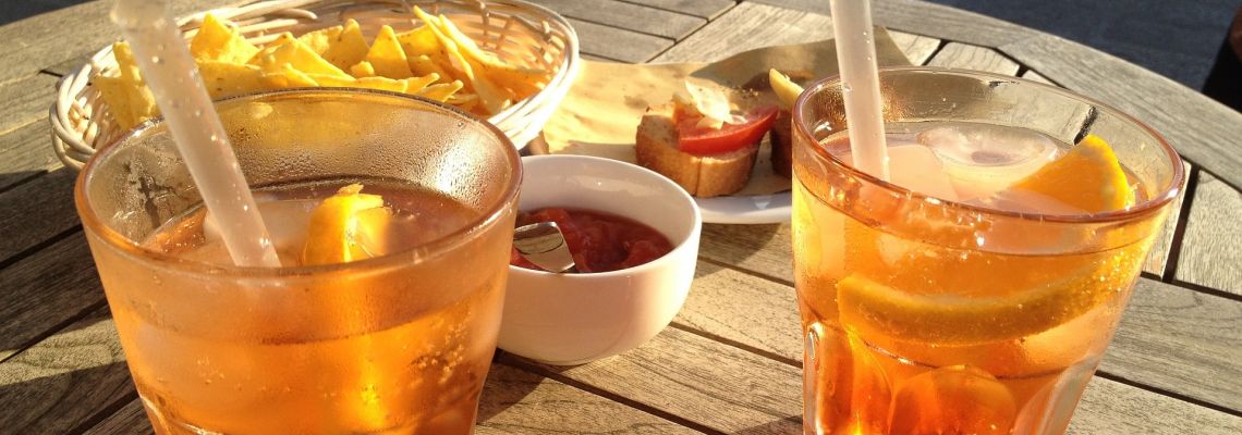 Twee glazen oranje aperitief met ijs en sinaasappel, naast schaaltjes met hapjes.