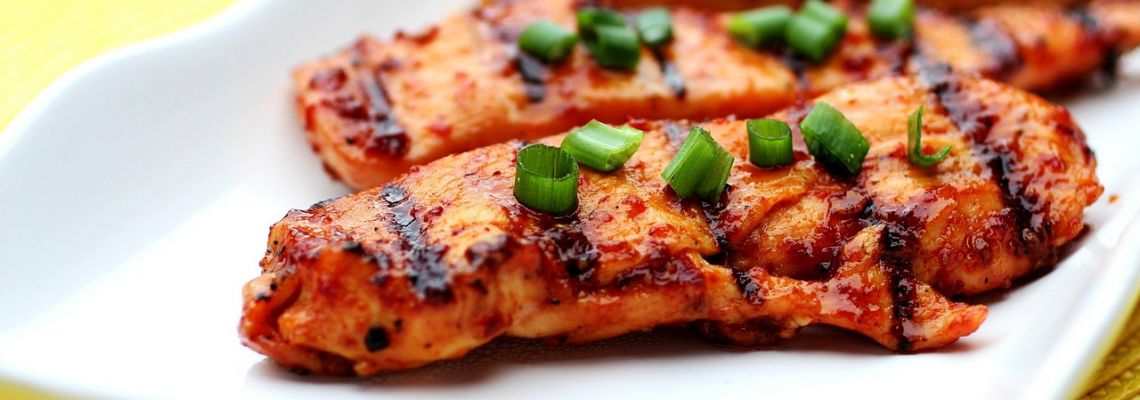 Gegrilde kipfilets met stukjes lente-ui op een wit bord.