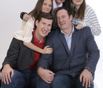 Twee mannen zitten naast elkaar, met drie kinderen achter hen.