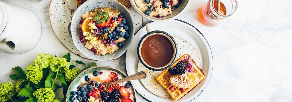 Ontbijttafel met kommen granen en fruit, een kop koffie en een wafel.
