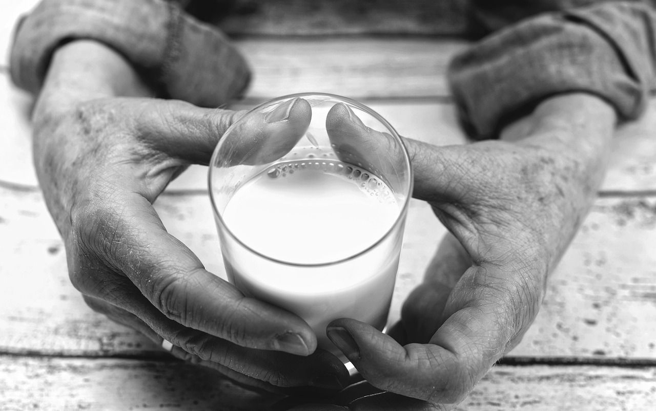 Oudere handen houden een glas melk vast boven een houten tafel.