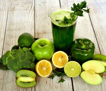 Een glas groen sap tussen broccoli, groene appels, paprika, kiwi en citrusvruchten.