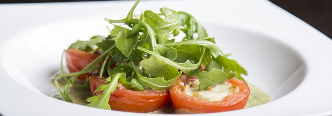 Tomaten met een witte kaasvulling en rucola op een wit bord.