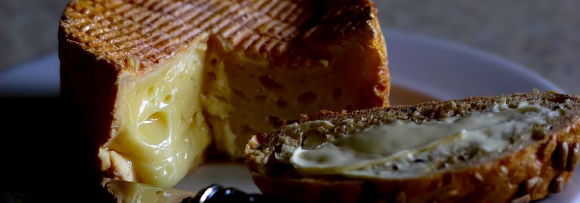 Een aangesneden zachte kaas met een smeuïge binnenkant, naast brood met kaas.