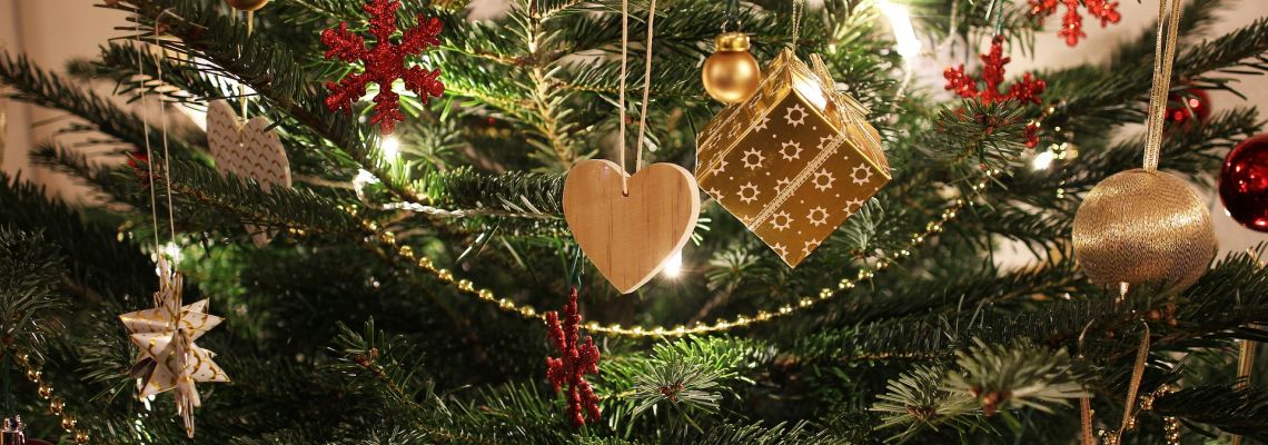 Een kerstboom met lichtjes, kerstballen, een houten hartje en andere versieringen.