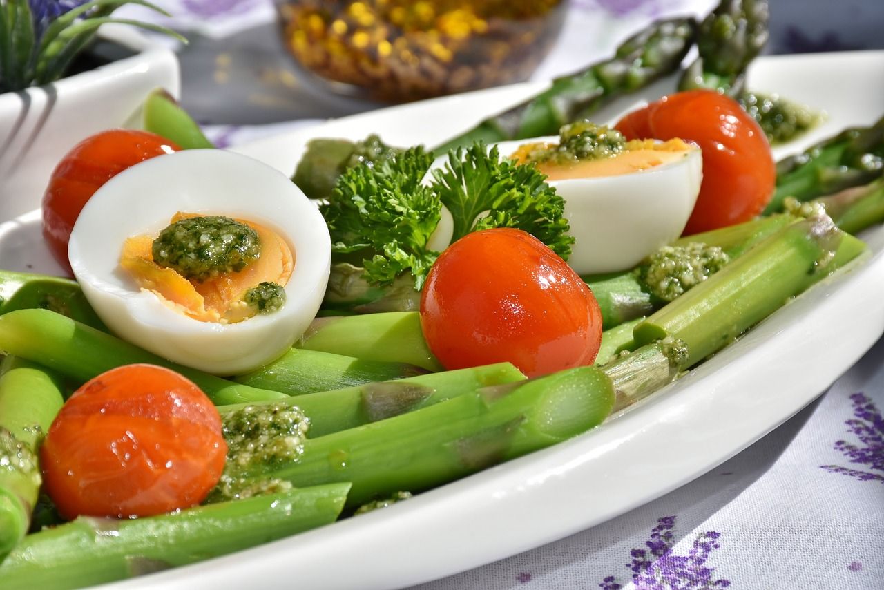 Groene asperges met gehalveerde gekookte eieren, kerstomaten en groene saus.