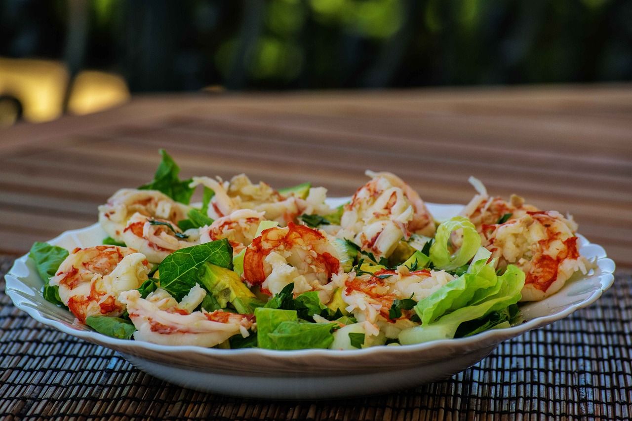 Een bord salade met rivierkreeftjes en sla op een houten tuintafel.