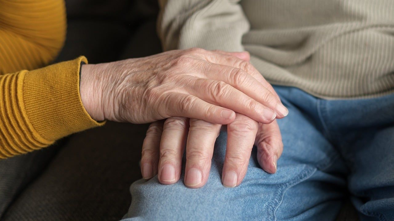 Een hand rust op de hand van een oudere persoon.