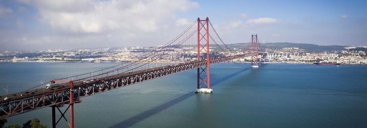 Rode hangbrug over breed water, met een stad op de heuvels op de achtergrond.