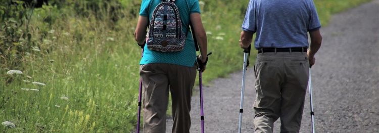 Twee mensen wandelen met wandelstokken op een pad langs het groen.