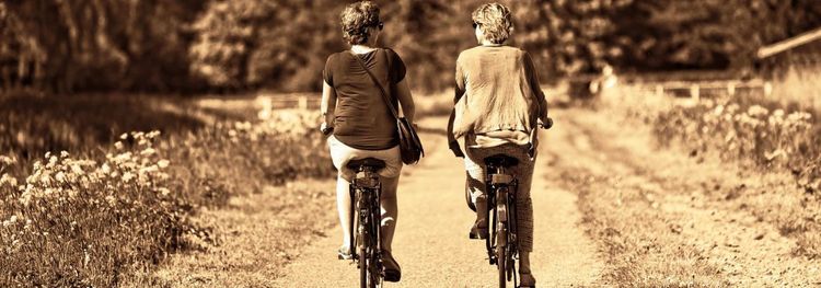 Twee mensen fietsen naast elkaar op een pad tussen gras en bloemen.