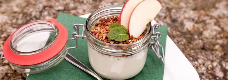 Glazen potje met yoghurt, granola, schijfjes appel en een blaadje munt.