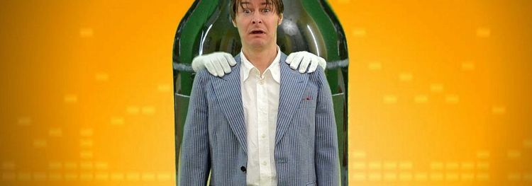 Man in een pak staat voor een grote groene fles, met witte handschoenen op zijn schouders.
