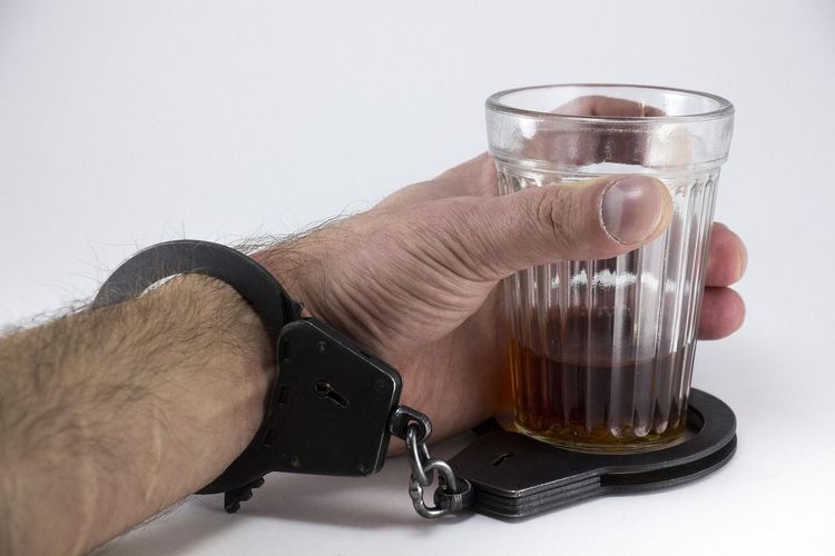 Een hand houdt een glas drank vast, met een handboei rond de pols en de andere rond het glas.