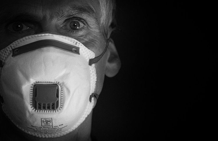 Een oudere man draagt een wit mondmasker in een zwart-witportret.