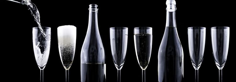 Champagneflessen en smalle glazen tegen een zwarte achtergrond. Eén glas wordt ingeschonken.