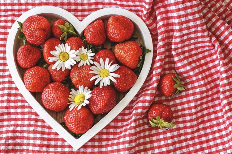 Aardbeien en madeliefjes in een hartvormige schaal op een rood-wit geruit tafelkleed.