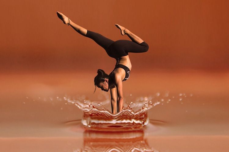 Een vrouw balanceert op haar handen met haar benen in de lucht, boven opspattend water.