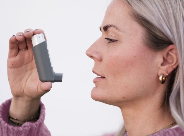 Een vrouw houdt een inhalator voor haar mond.