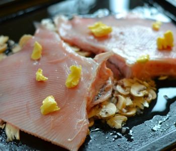 Rogvleugels met klontjes boter op een bedje van gesneden champignons.