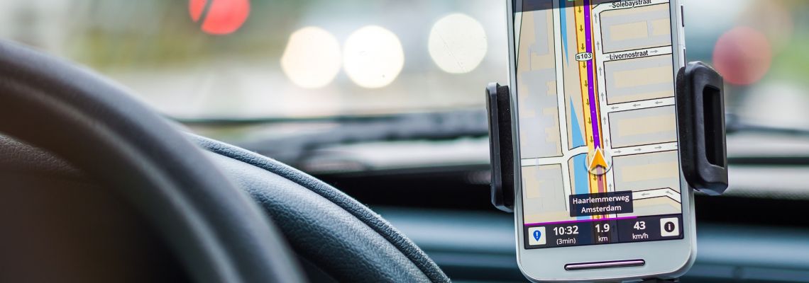 Smartphone in een houder naast het stuur van een auto, met een navigatiekaart op het scherm.