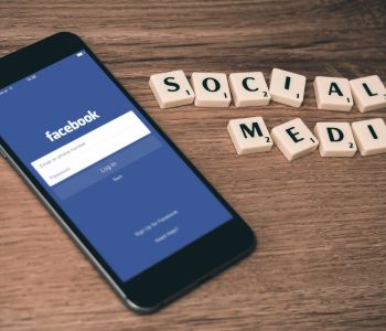 Smartphone met het inlogscherm van Facebook naast houten letterblokjes op een tafel.