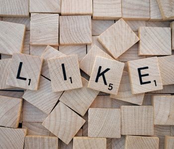 Houten letterblokjes vormen het woord LIKE tussen andere blokjes.