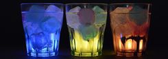 Drie glazen met gekleurde drankjes en ijsblokjes, van onderen verlicht.