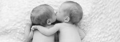 Twee baby's liggen dicht tegen elkaar, met een armpje om elkaar heen.