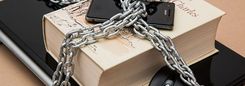 Een ketting ligt rond een dik boek, een smartphone en een laptop.