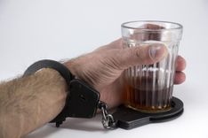 Een hand houdt een glas drank vast, met een handboei rond de pols en de andere rond het glas.