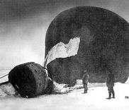 Zwart-witbeeld van een neergekomen luchtballon met een mand en twee mensen in de sneeuw.