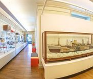 Museumzaal met een scheepsmodel in een glazen vitrinekast.