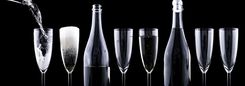 Champagneflessen en smalle glazen tegen een zwarte achtergrond. Eén glas wordt ingeschonken.