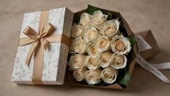 Een geschenkdoos met een grote gouden strik naast een boeket witte rozen.