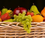 Een rieten mand vol fruit, met groene druiven, appels, peren, aardbeien en een sinaasappel.