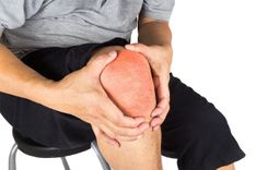 Een zittende persoon houdt met beide handen een rood gekleurde knie vast.