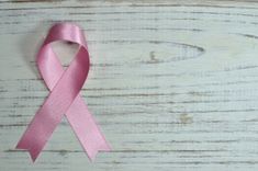Roze lintje als symbool voor borstkanker op een witgeverfde houten achtergrond.