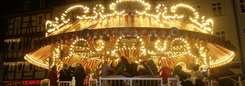 Draaimolen met warme lichtjes tussen vakwerkhuizen op een kerstmarkt.