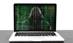 Een laptop met groene computercode en een donkere figuur met een kap op het scherm.