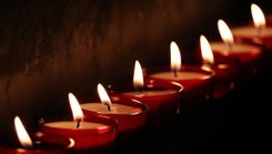Een rij brandende kaarsjes in rode houders verlicht de donkere ruimte.