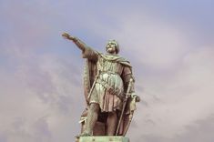 Een standbeeld van een man in een harnas en mantel, met één arm uitgestrekt.